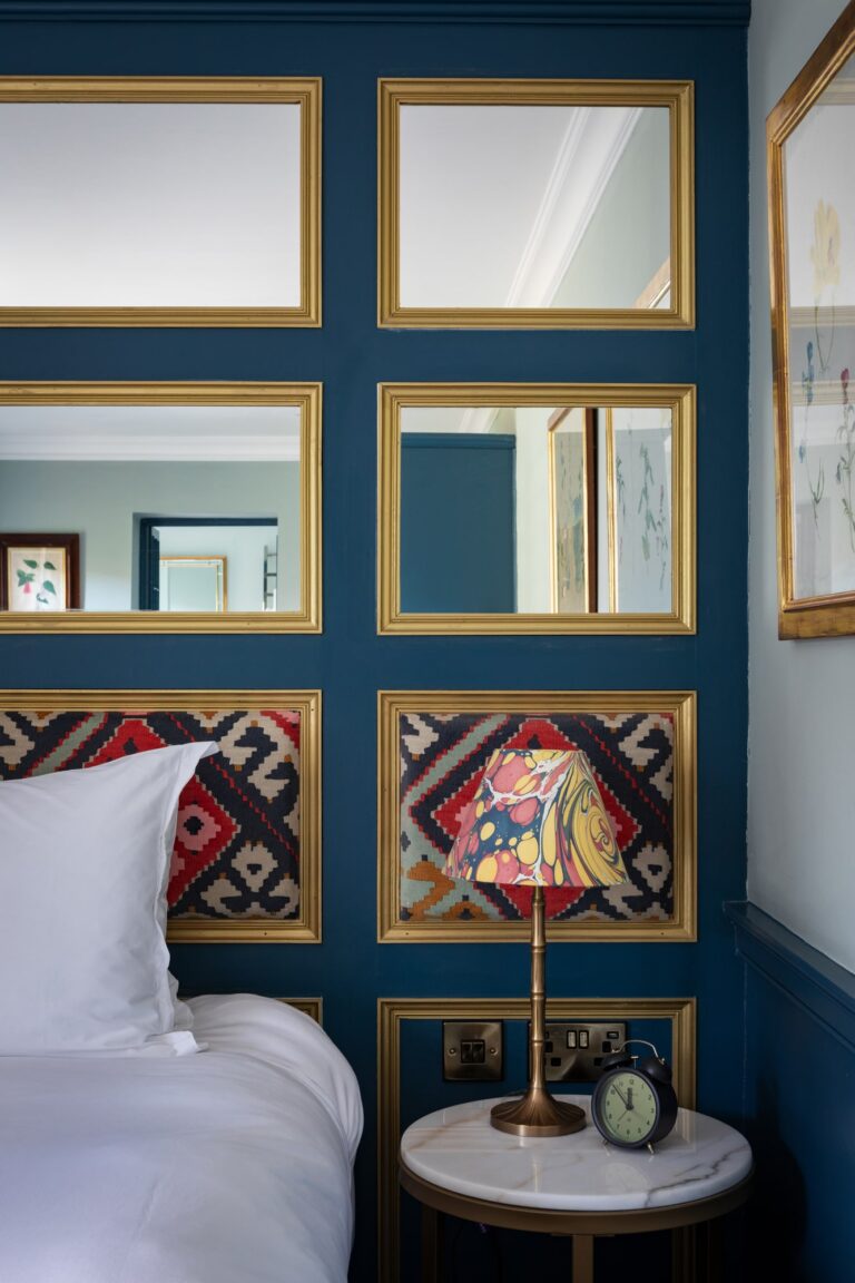 A large double bedroom, with blue walls and a large roll top bath with mirrors on the walls and antique furnishings.