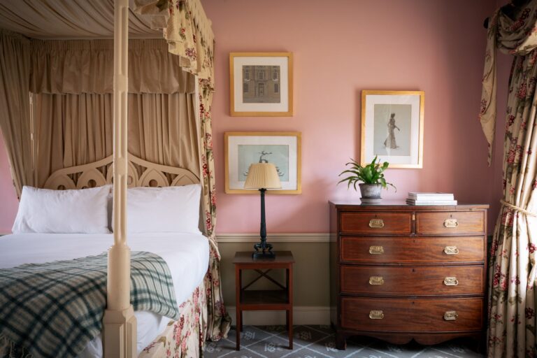 A fourposter bed in a pink room with antique furnishings.