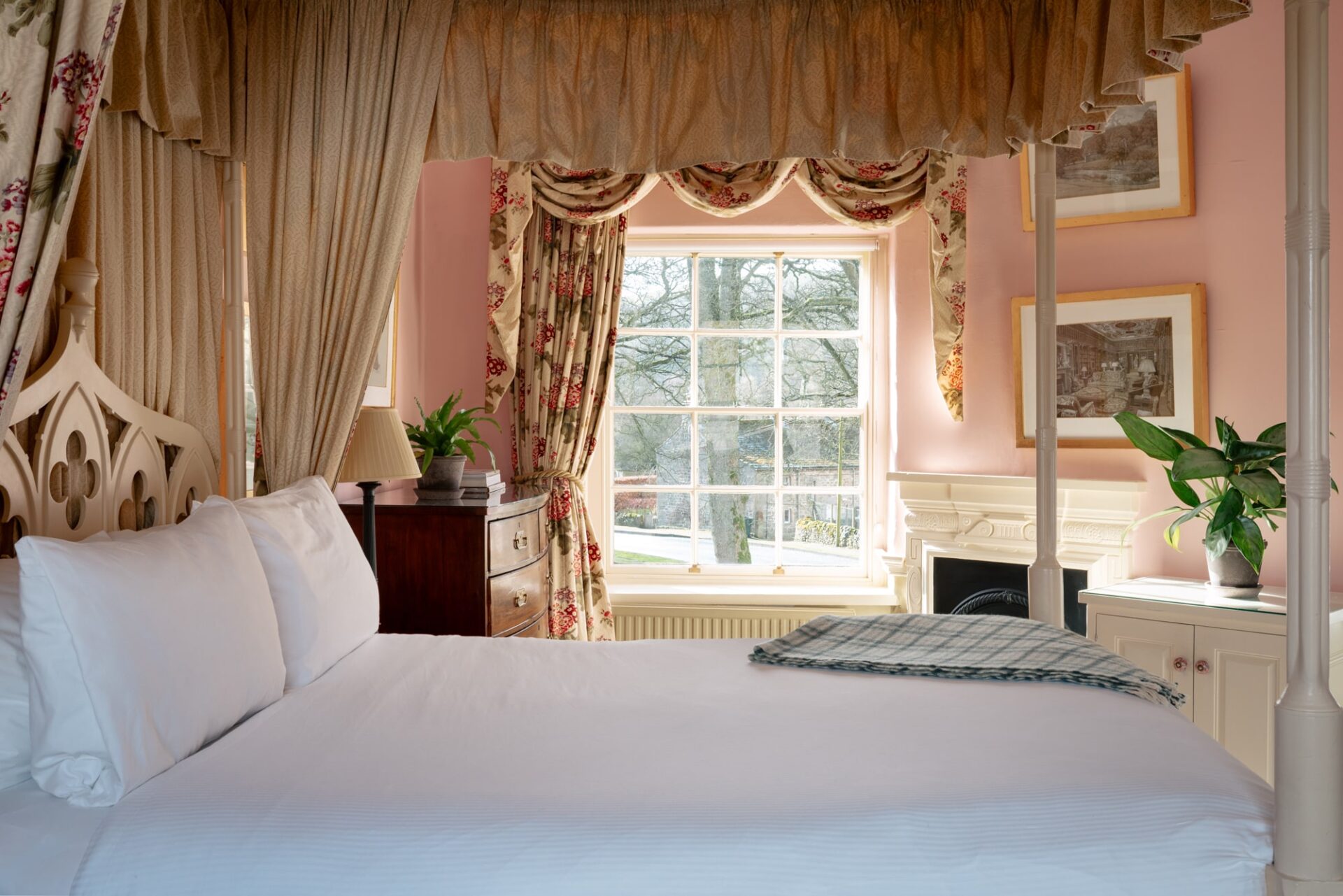 A large fourposter bedroom with pink walls and floral curtains, with antique furnishings.
