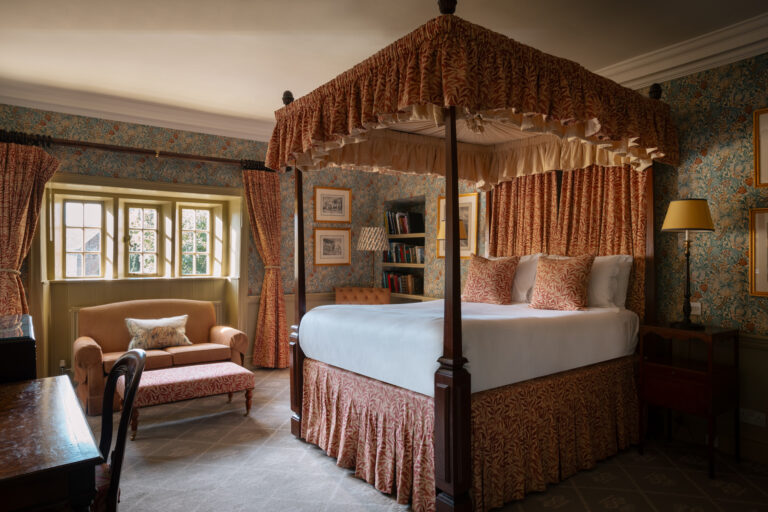 A large fourposter bedroom with blue and red floral furnishings and walls, and antiques dotted about.