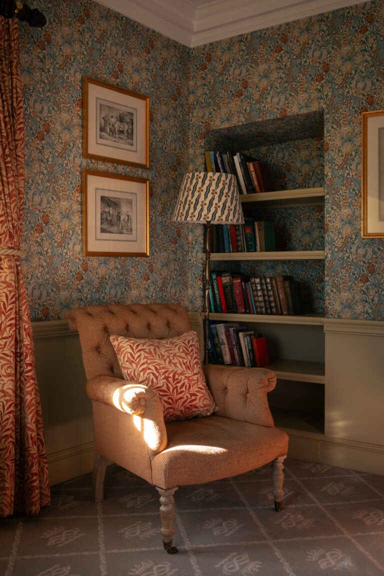 A large fourposter bedroom with blue and red floral furnishings and walls, and antiques dotted about.