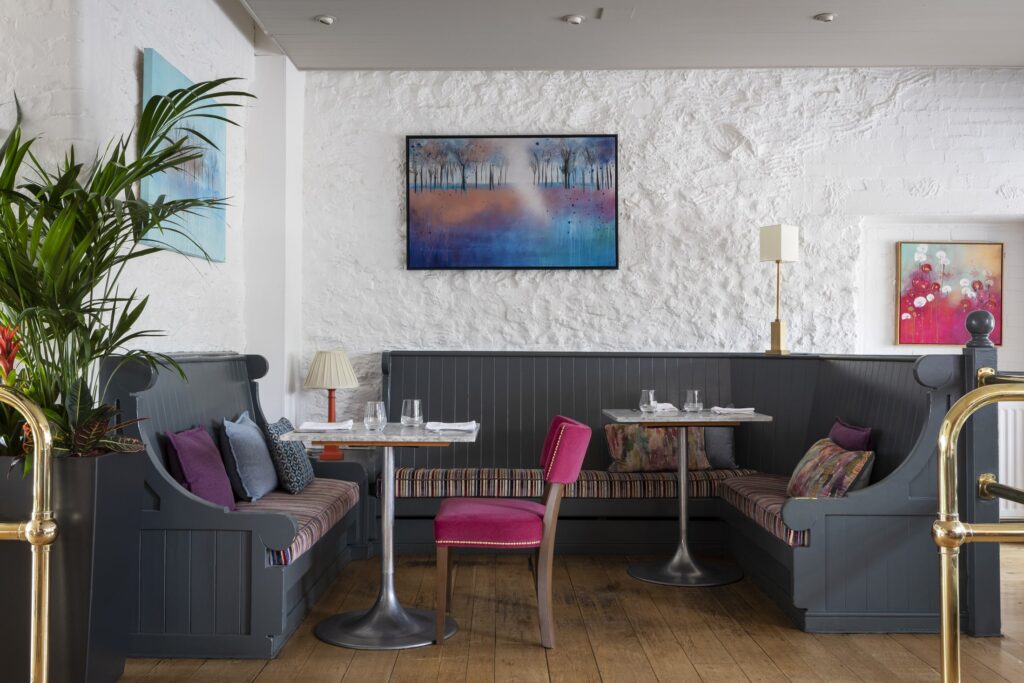 A large room set with colourful dining chairs and tables, with open windows and plants.