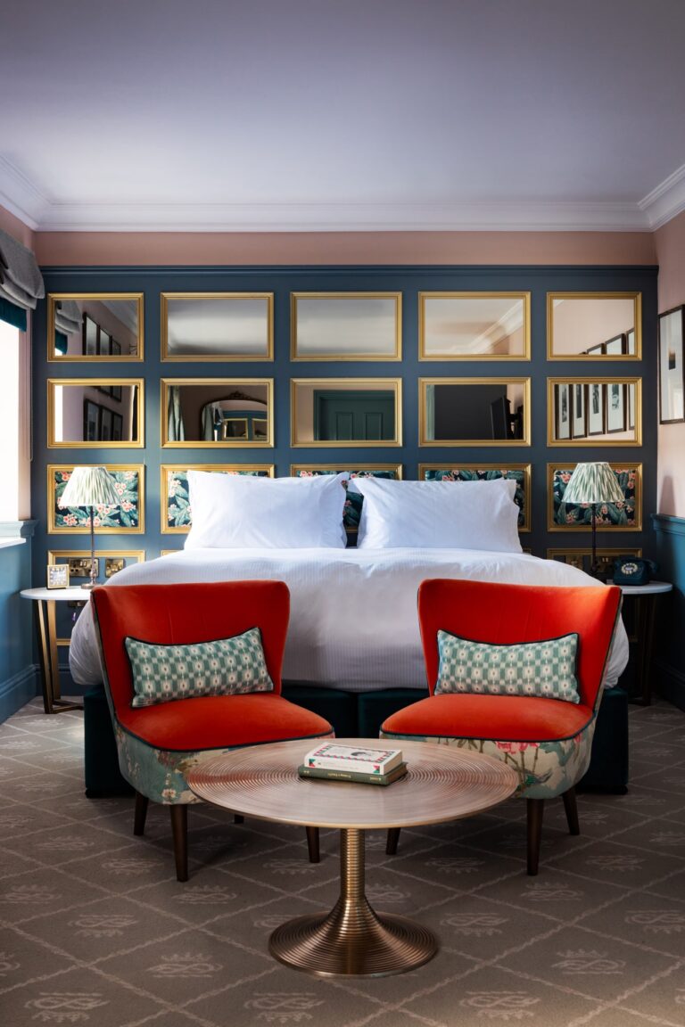 A large double bedroom with orange and blue walls, mirrors on the walls and antique furnishings.