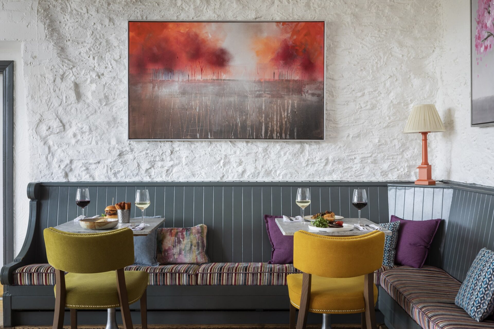 A large room set with colourful dining chairs and tables, with open windows and plants.