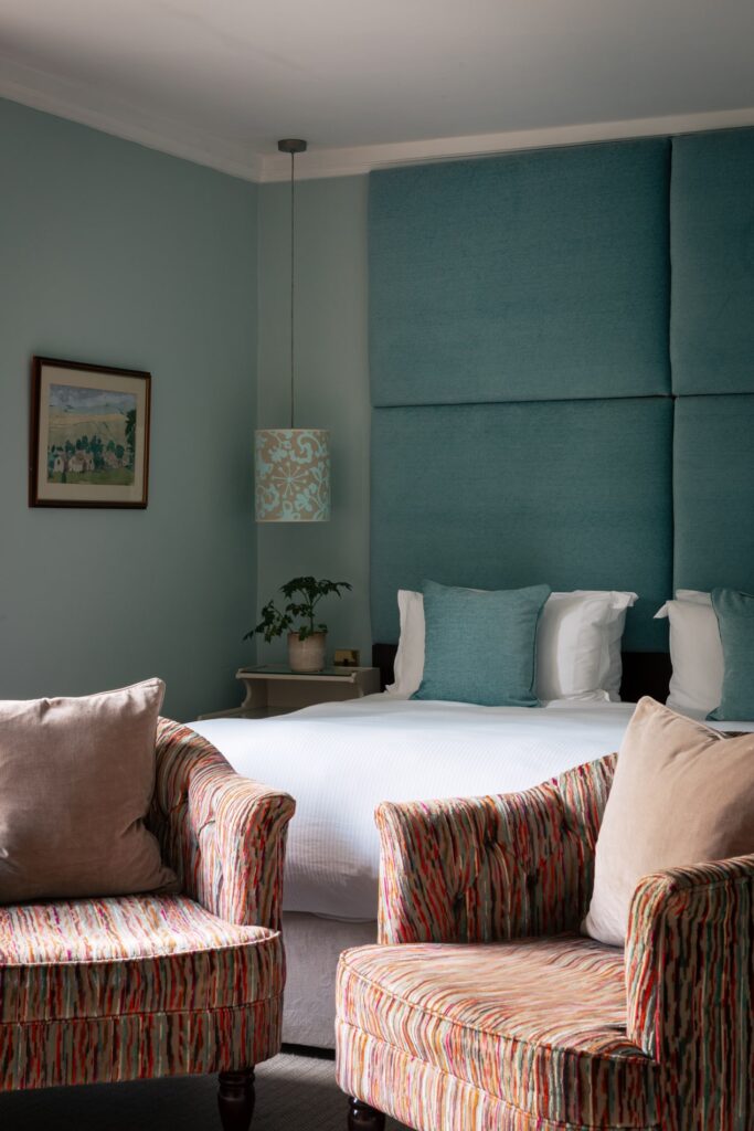 A blue bedroom with large blue headboard and hanging ceiling lights.