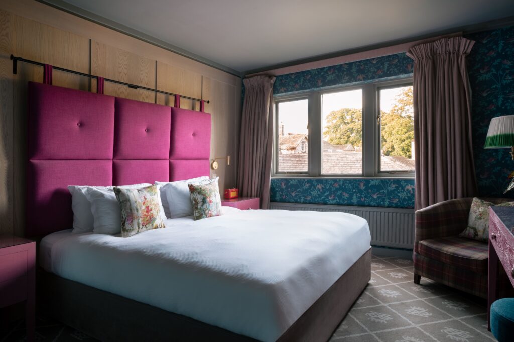 A bedroom with wooden panelling and a pink headboard, and blue floral wallpaper.