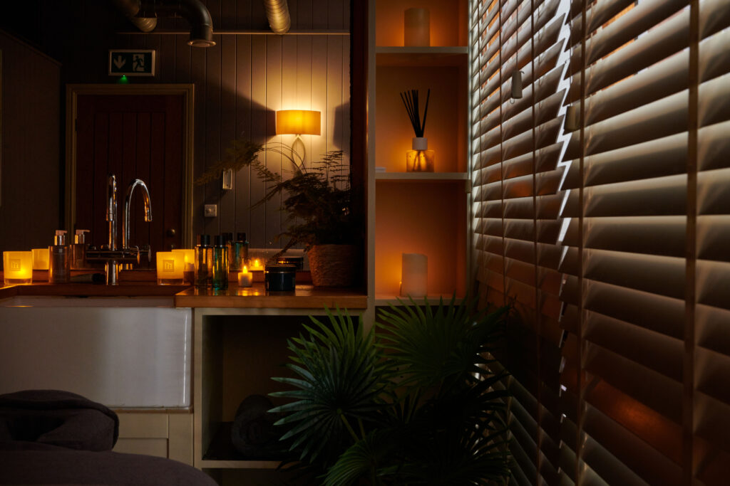 A peaceful spa treatment room with candles and mood lights and products and plants.