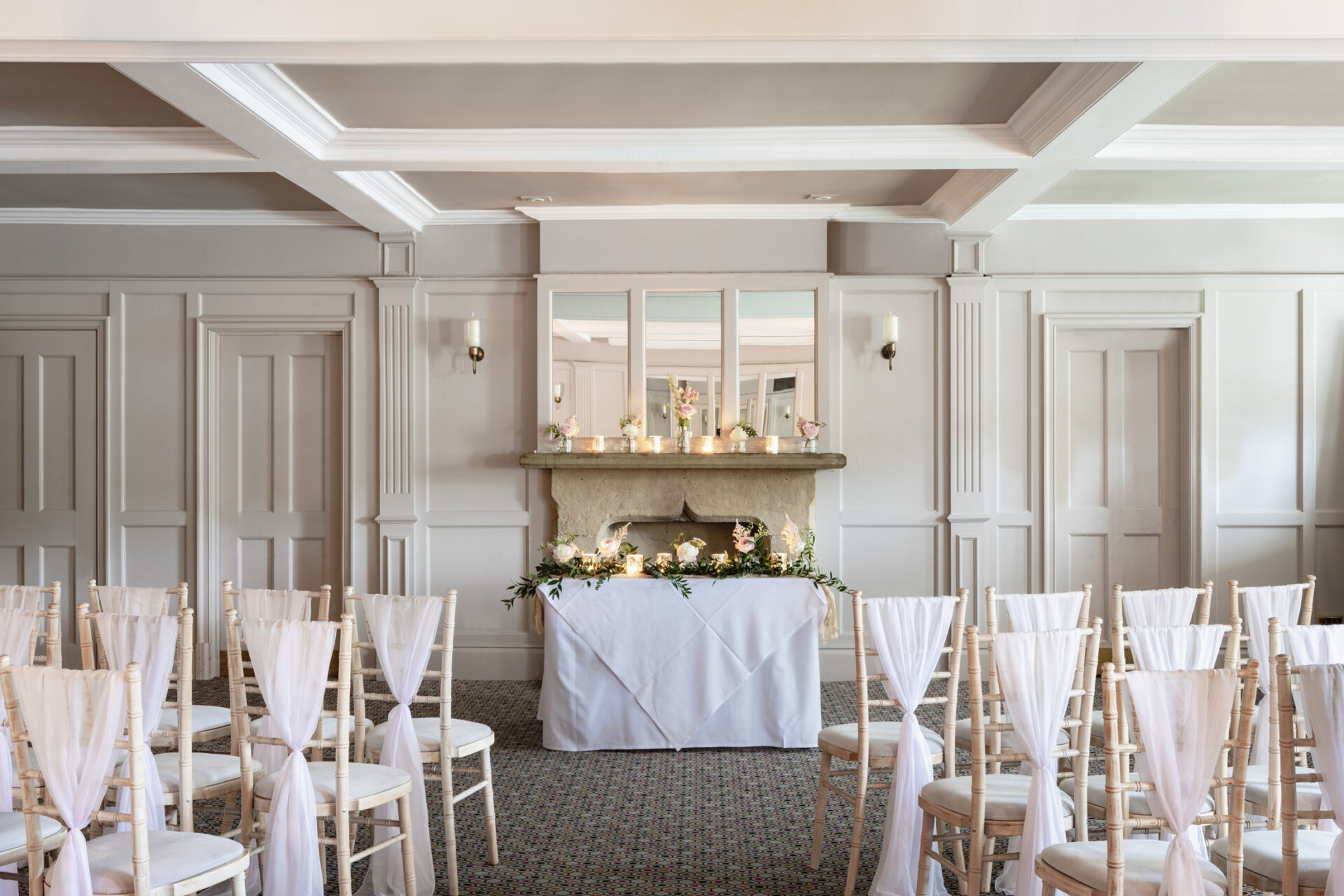 panelled wall with white tablecloths, candles and chairs for a wedding ceremony