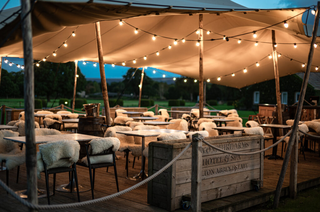 The outside terrace at dusk, with lights and fluffy throws on the outside chairs and tables.