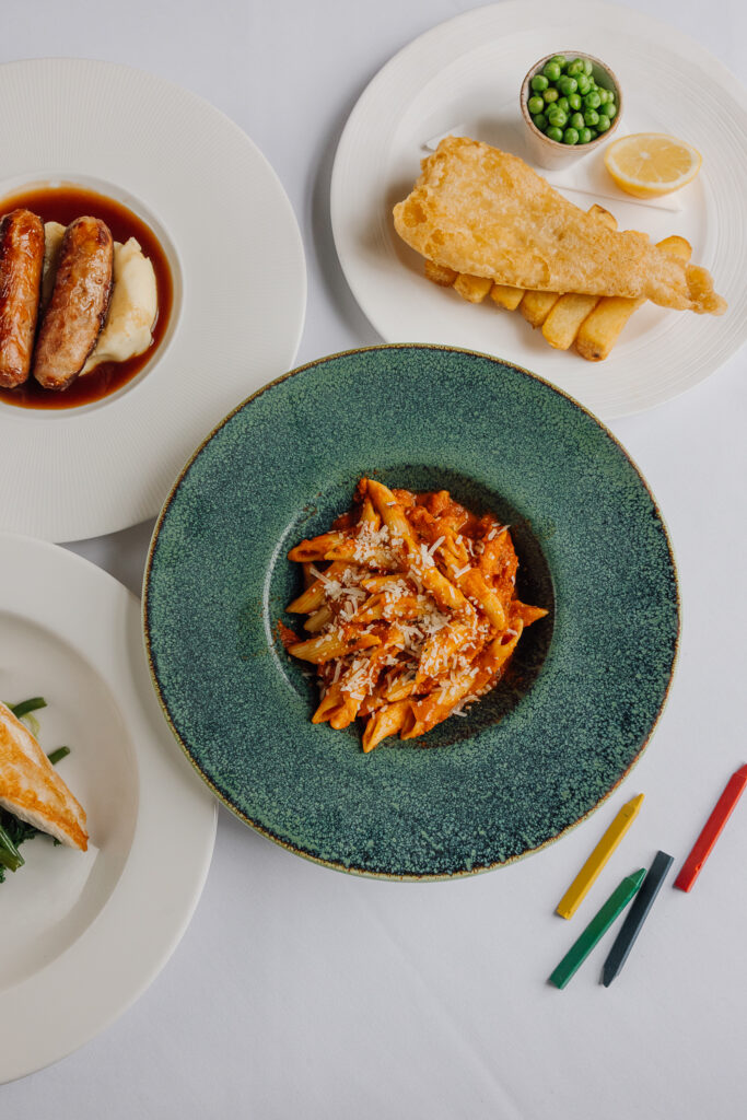 Tomato pasta, fish and chips, sausage and mash. Colouring crayons laying on the table.