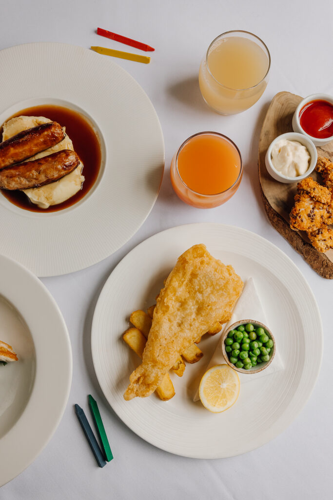 Small plates of fish and chips, sausage and mash potato and chicken tenders. Drinks and colouring crayons.