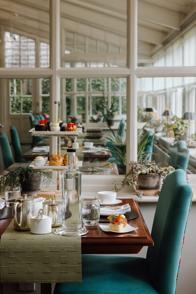 A luxurious afternoon tea stand in The Garden Room filled with sandwiches, sweet treats and scones. A large pot of tea also lays on the table.