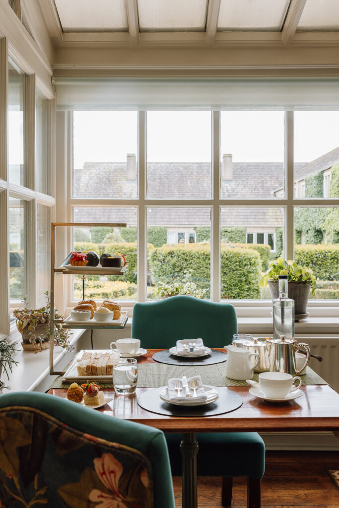 A luxurious afternoon tea stand in The Garden Room filled with sandwiches, sweet treats and scones. A large pot of tea also lays on the table. The table looks over the Italian Gardens.