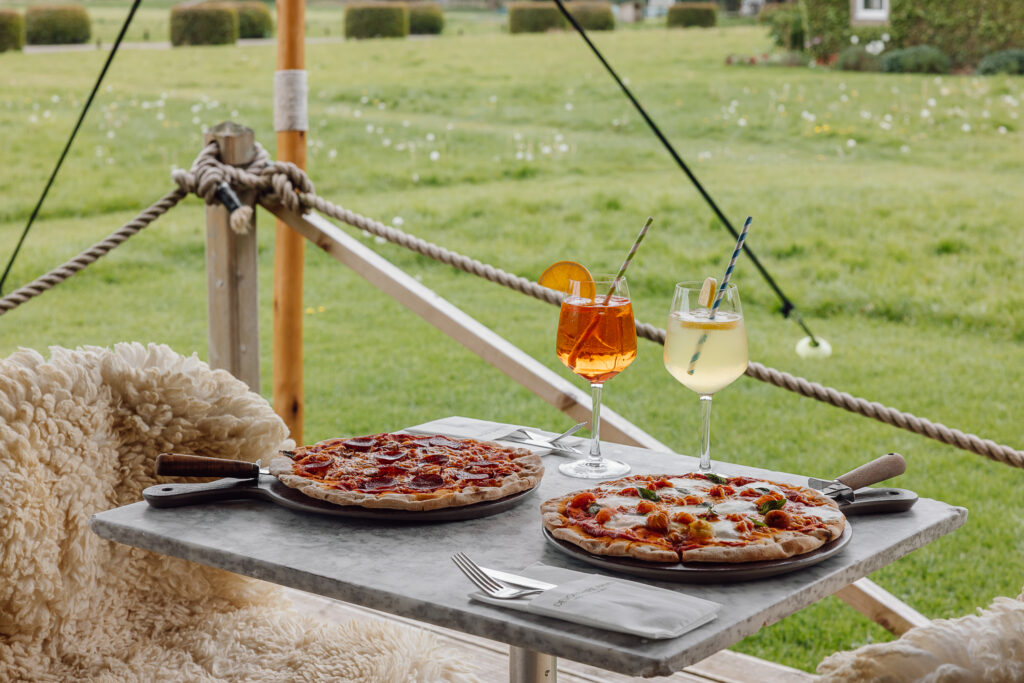 Two pizzas on a table with two spritz drinks