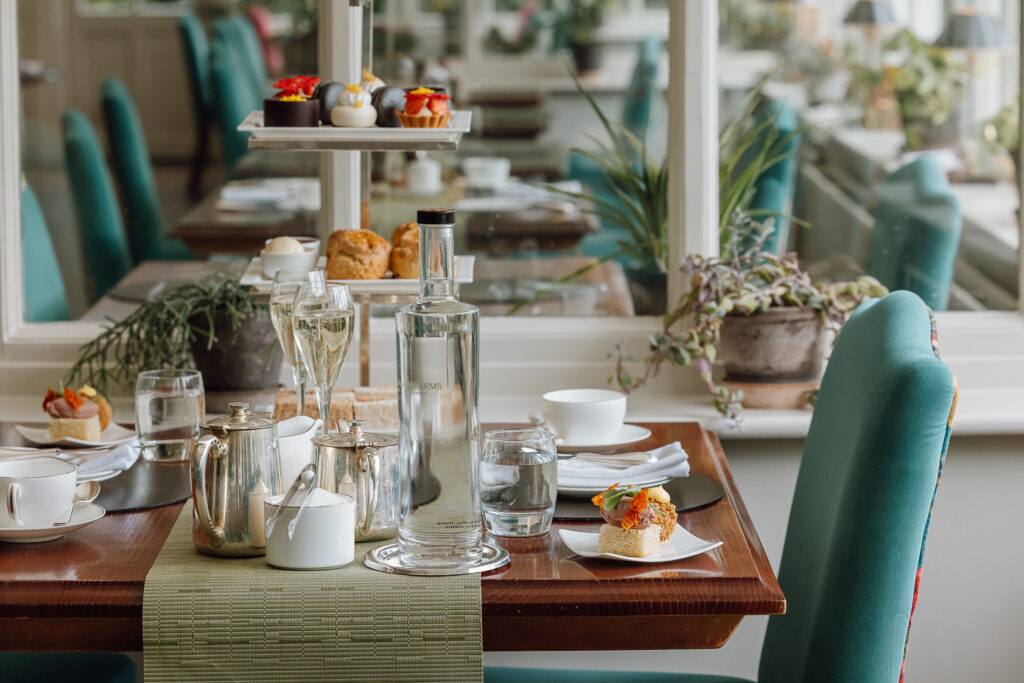A luxurious afternoon tea stand in The Garden Room filled with sandwiches, sweet treats and scones. A large pot of tea also lays on the table.